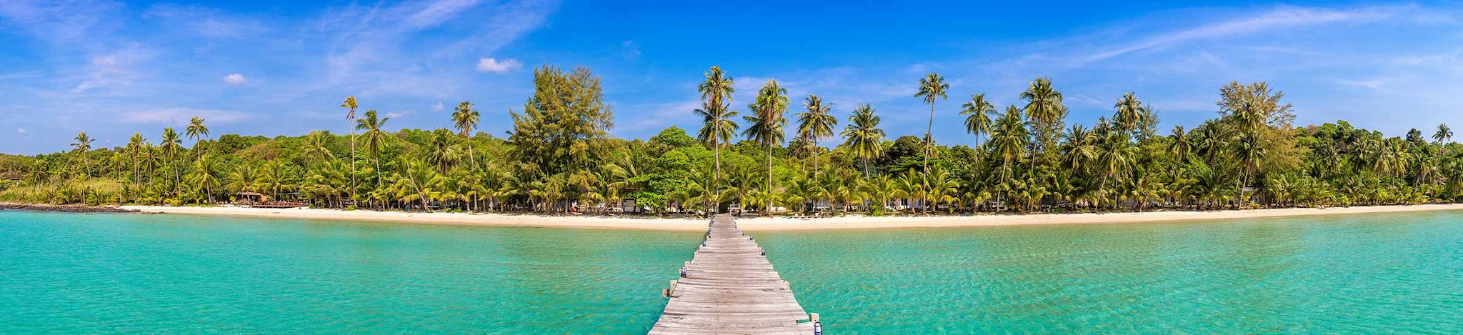 Blick auf einen Steg im Meer mit Strand und Palmen im Hintergrund